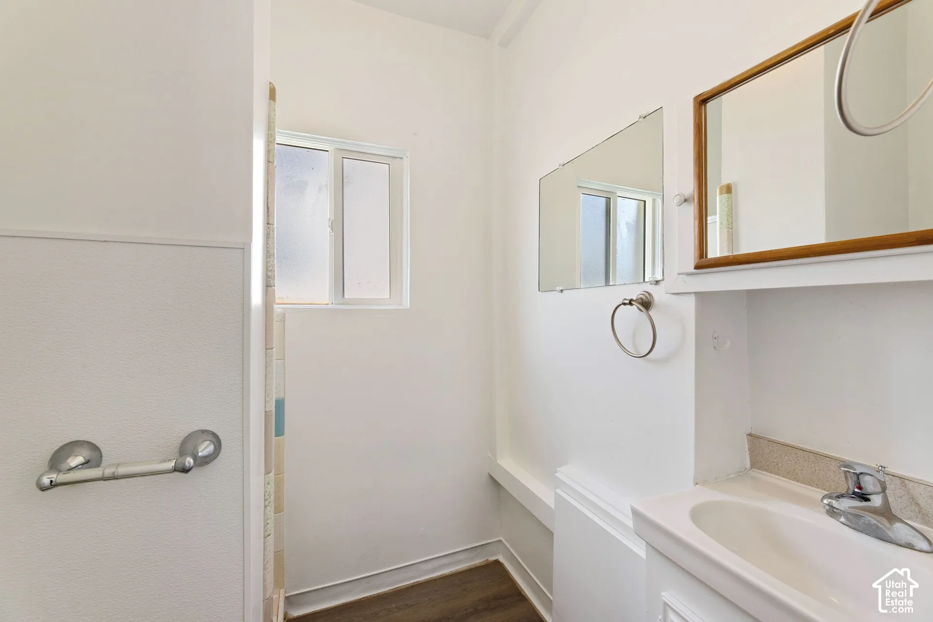 ADU Bathroom featuring a single vanity with a ceramic sink, a chrome faucet, a wooden framed mirror, and a frosted window