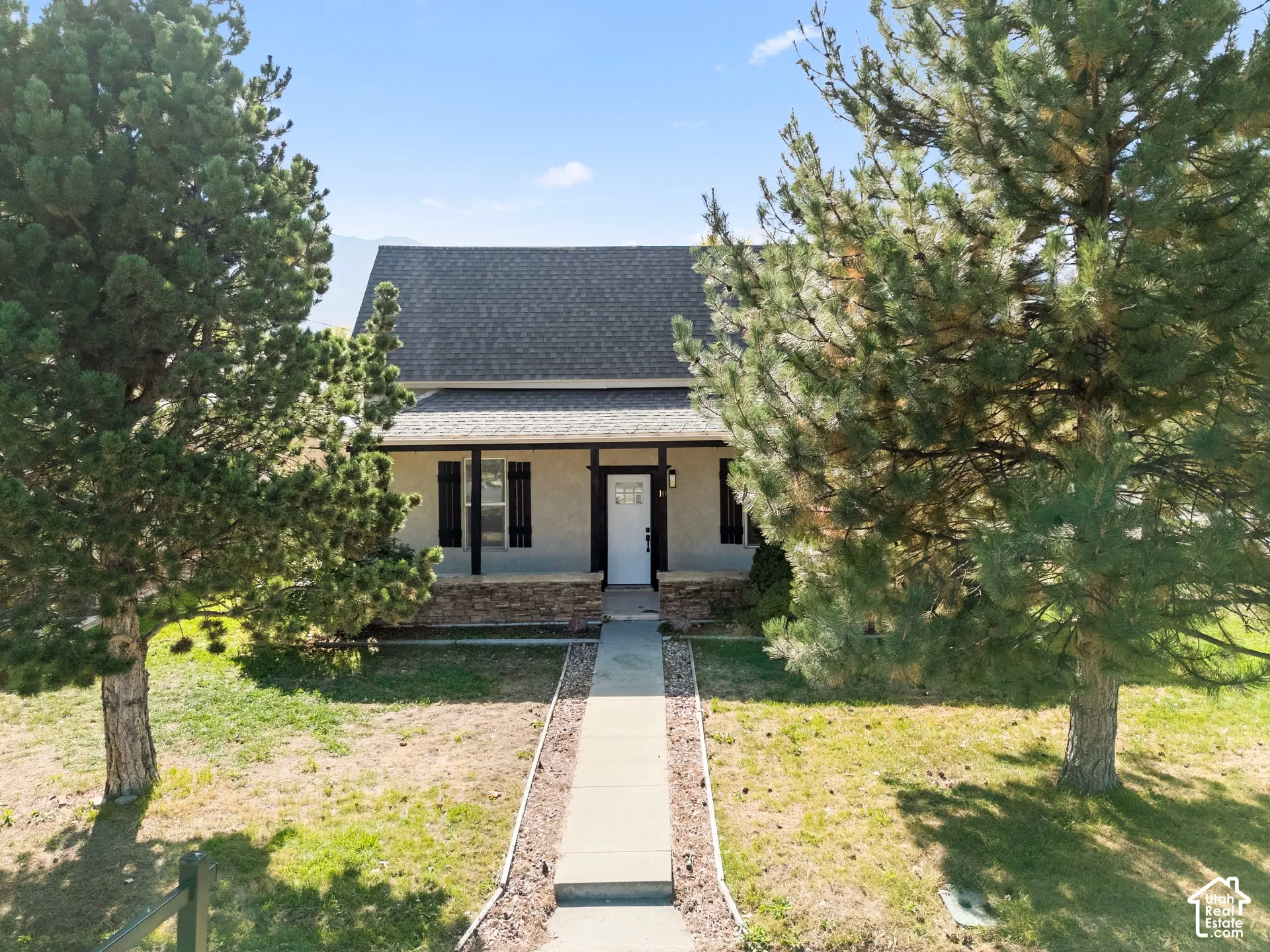 Stucco exterior with a dark shingle roof and a covered front porch featuring stone accents