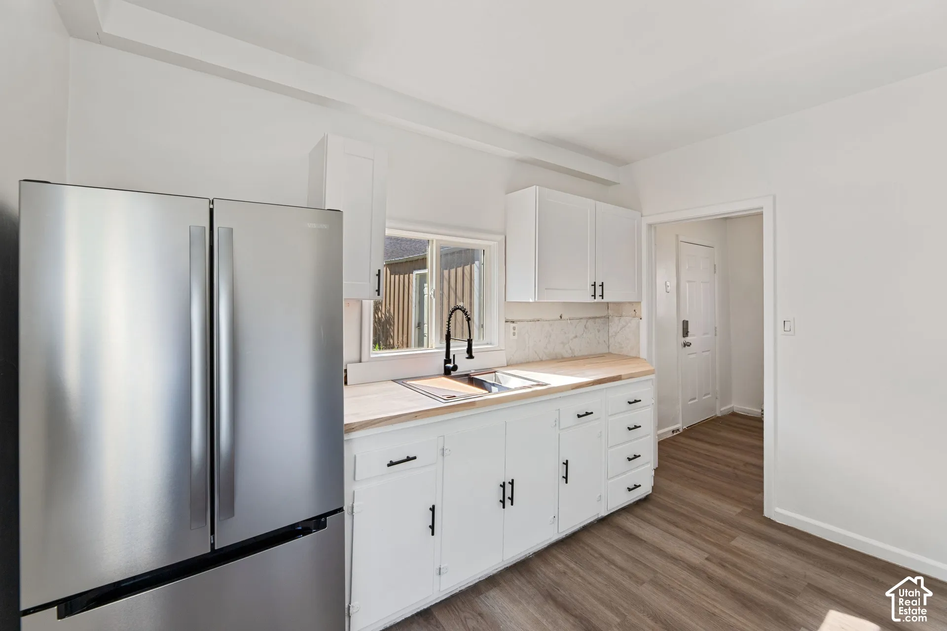 ADU with New Stainless steel refrigerator, white cabinetry with dark hardware, wood-finish countertops, undermount sink with a matte black faucet, and wood-finish flooring