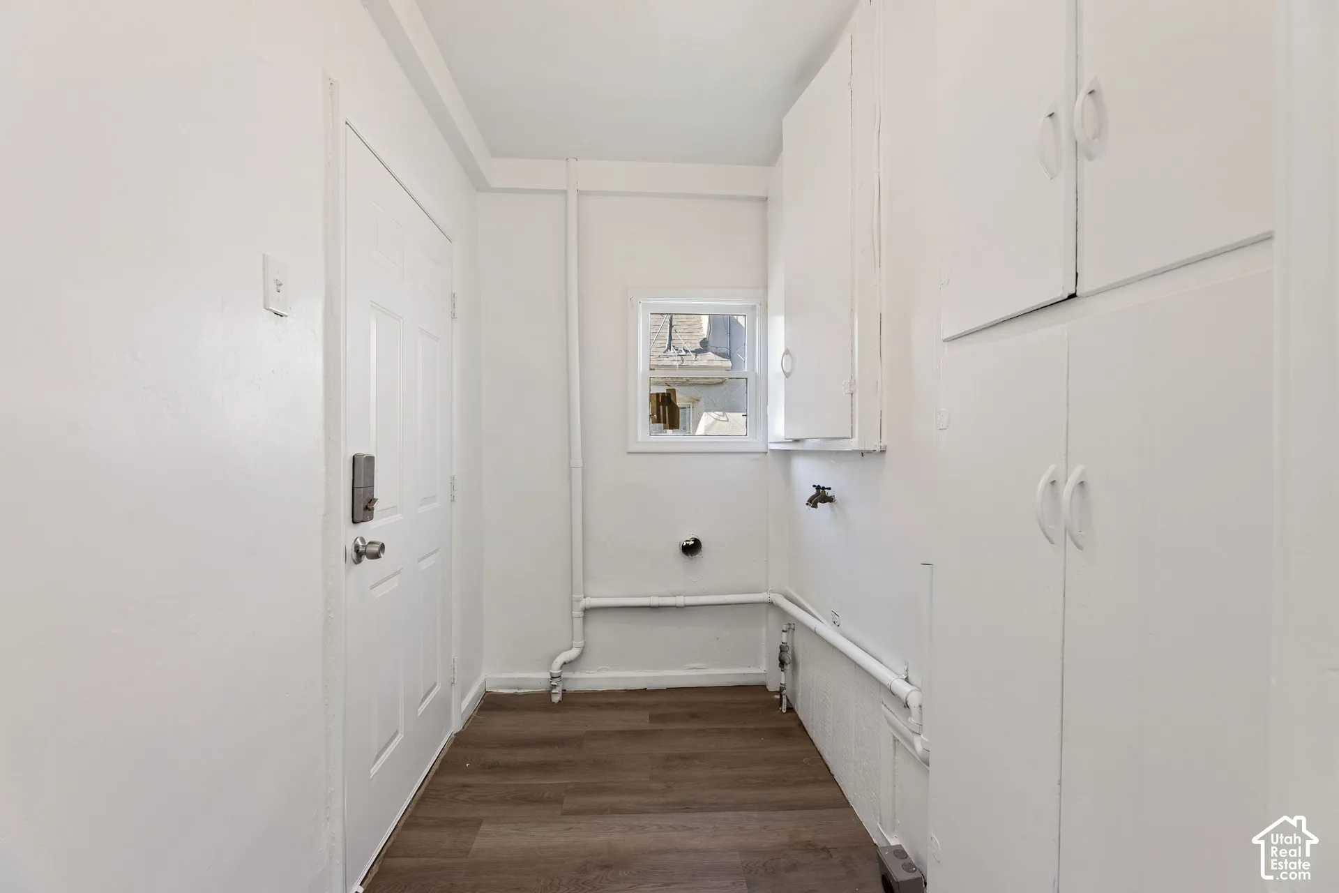 ADU Laundry Room with White cabinetry, wood-finish flooring, white paneled door with exit to backyard, and a small window