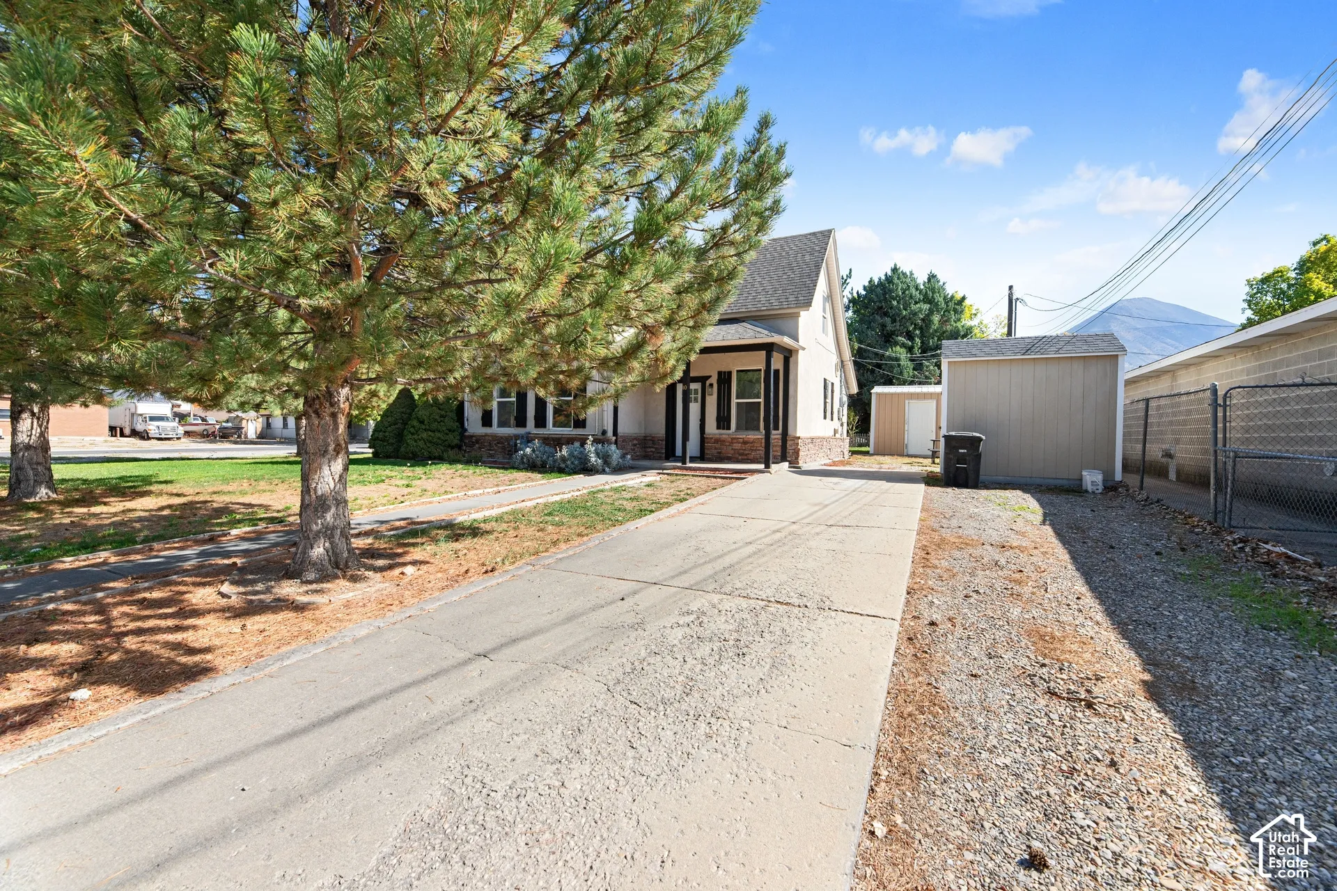 Gabled roofline, stone facade accent, covered porch entry, paved driveway, and detached storage shed