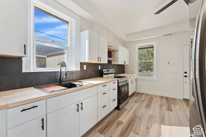 Main House New Kitchen with White shaker cabinetry with black hardware, wood-finish countertops, dark tile backsplash, stainless steel range, and wood-finish flooring