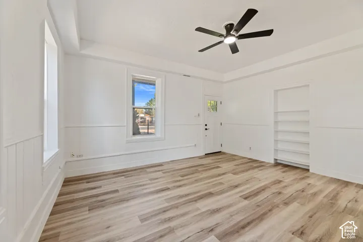 Main House Wood-finish flooring, white wainscoting, built-in shelving, ceiling fan with integrated lighting, and multiple windows