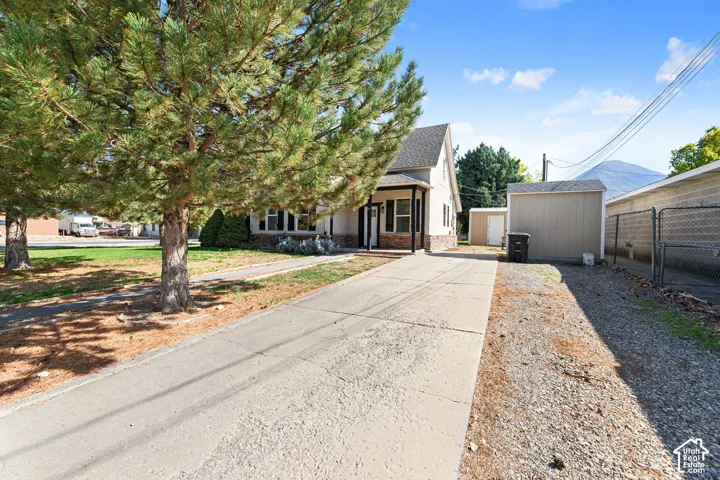 Gabled roofline, stone facade accent, covered porch entry, paved driveway, and detached storage shed