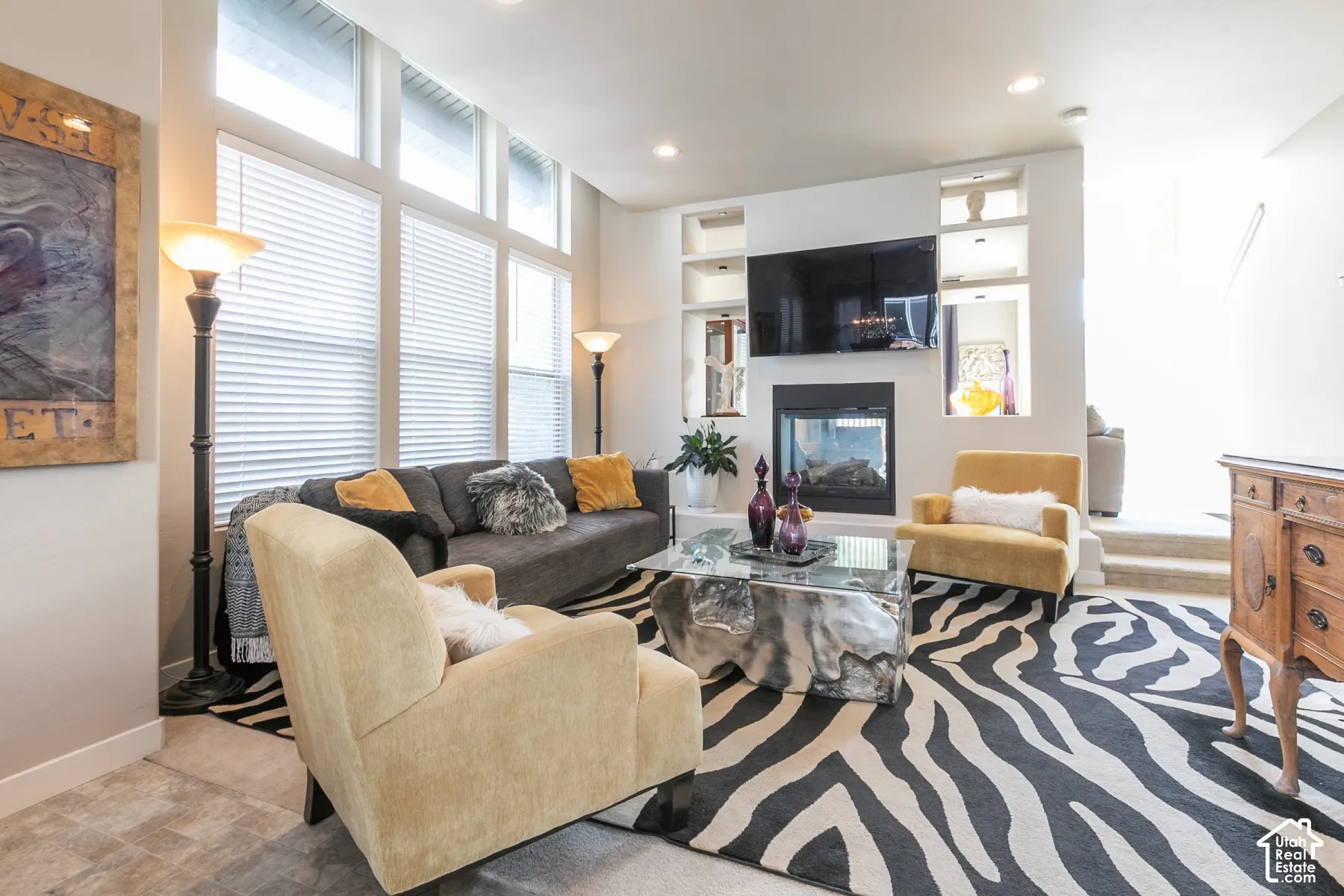 Living area featuring a modern fireplace, built-in shelving, large windows with blinds, and recessed lighting