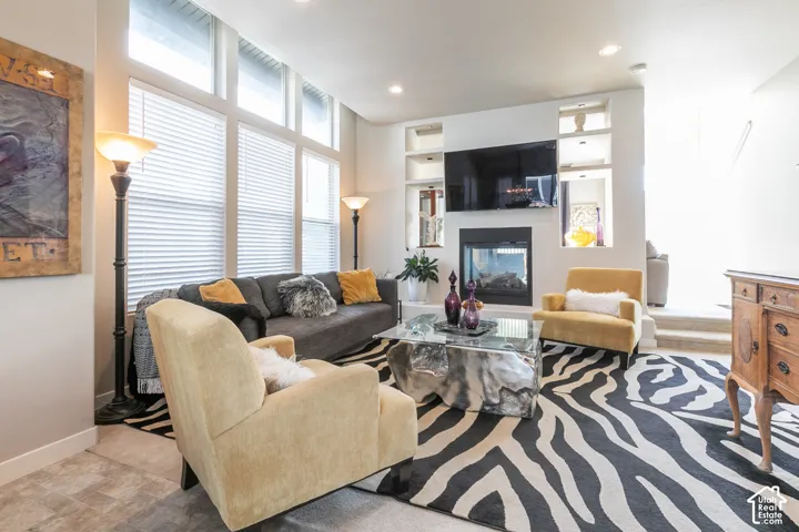 Living area featuring a modern fireplace, built-in shelving, large windows with blinds, and recessed lighting