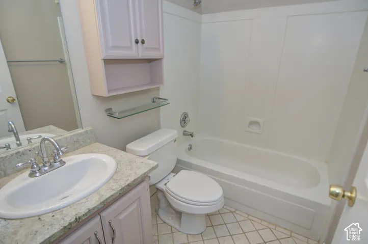 Bright bathroom featuring a round pedestal sink with polished chrome faucet and granite countertop, an alcove bathtub with tile surround, a toilet with elongated bowl, and overhead cabinetry with shelving for storage