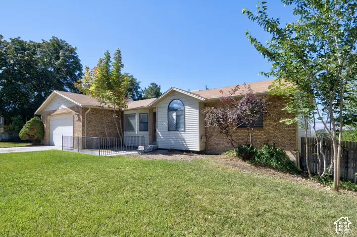 Brick and siding exterior with a pitched roof, attached garage, arched window, and front yard with mature landscaping