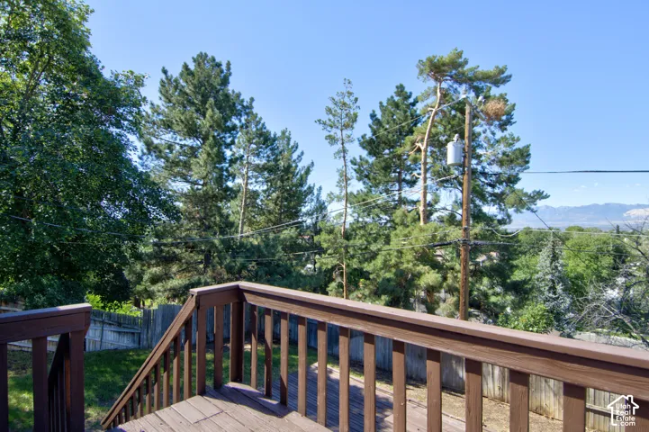 Wood-finish deck with a brown railing, surrounded by mature trees, and a distant mountain backdrop