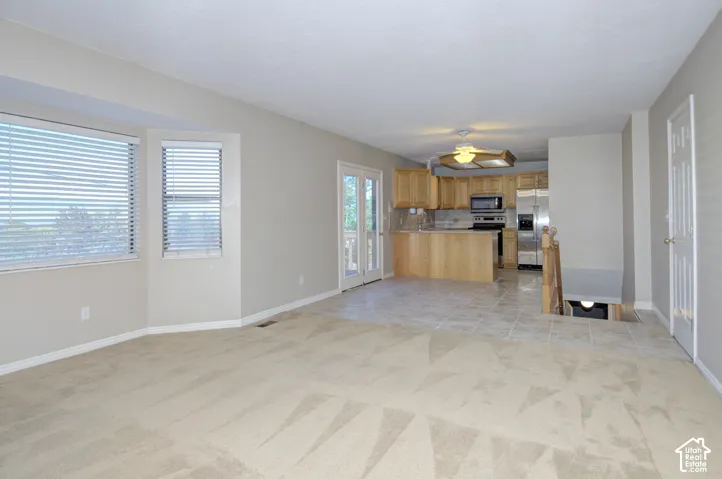 Spacious open-concept living area featuring wood-finish flooring throughout, abundant natural light from multiple windows with plantation shutters, and a fully equipped kitchen with wood cabinetry and stainless steel appliances