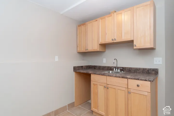 Light wood-finish cabinetry, stainless steel sink, dark countertop, and tiled flooring