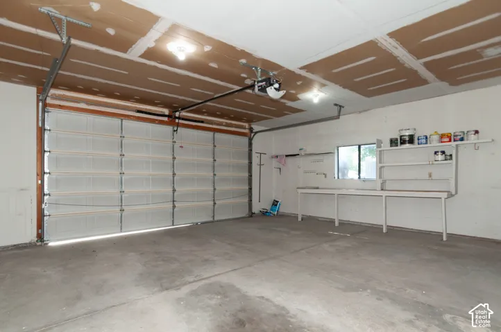 Spacious garage featuring a large overhead door, automatic opener, concrete flooring, and built-in shelving with a workbench