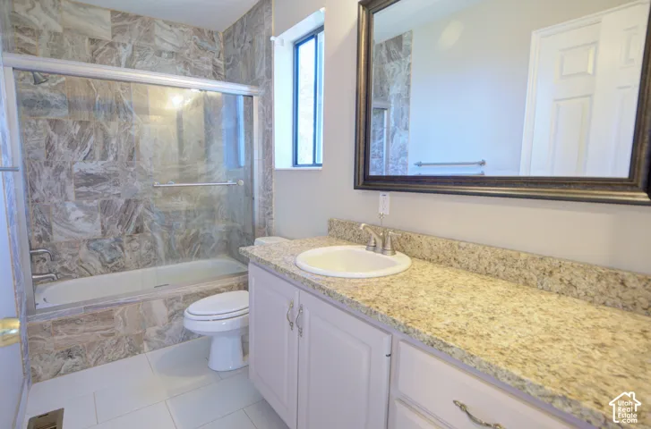 Full-size bathtub with glass shower enclosure, extensive tile surround, vanity with light-colored countertop, and a framed mirror