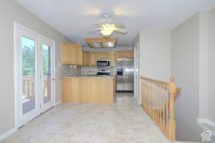 Kitchen area featuring tiled flooring, wood cabinetry, stainless steel appliances, and a ceiling fan