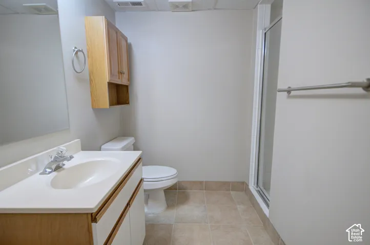 Bathroom featuring a vanity with a white countertop and basin, wood-finish cabinetry, a mirror, and a shower with a clear enclosure