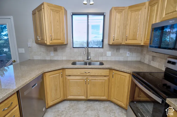 Wood-finish cabinetry, stainless steel sink, tile flooring, and tile backsplash