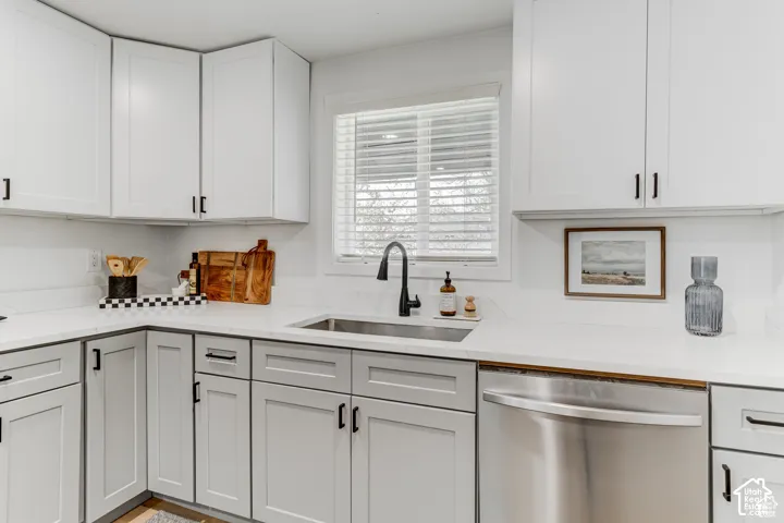 Modern kitchen featuring white upper cabinetry, gray lower cabinetry, stainless steel sink, black faucet, and stainless steel dishwasher