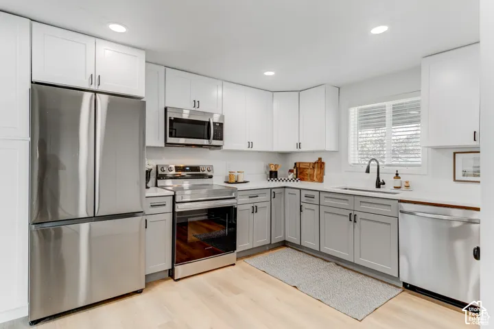 Updated kitchen featuring stainless steel appliances, light wood-finish flooring, white upper cabinetry, grey lower cabinetry, and recessed lighting