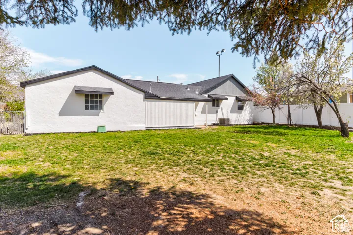 Expansive backyard featuring a manicured lawn, white privacy fencing, mature trees, and a stucco exterior