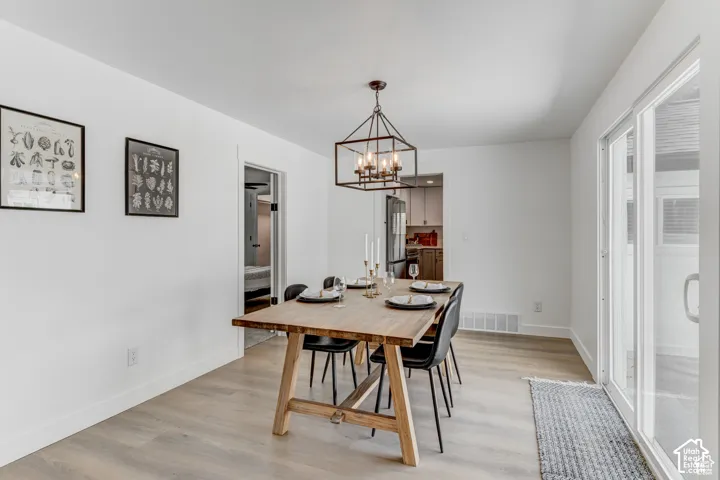 Dining area featuring wood-finish flooring, white walls, and a contemporary chandelier