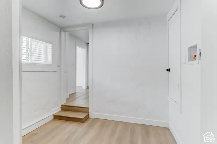 Light wood-finish flooring, white painted walls, window with blinds, and laundry connections