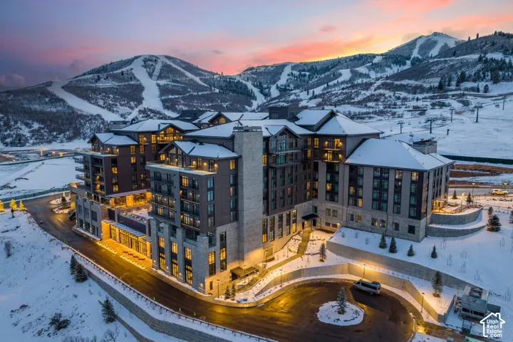 Multi-story building featuring stone and wood-look cladding, multiple balconies, and a circular drive with landscape lighting