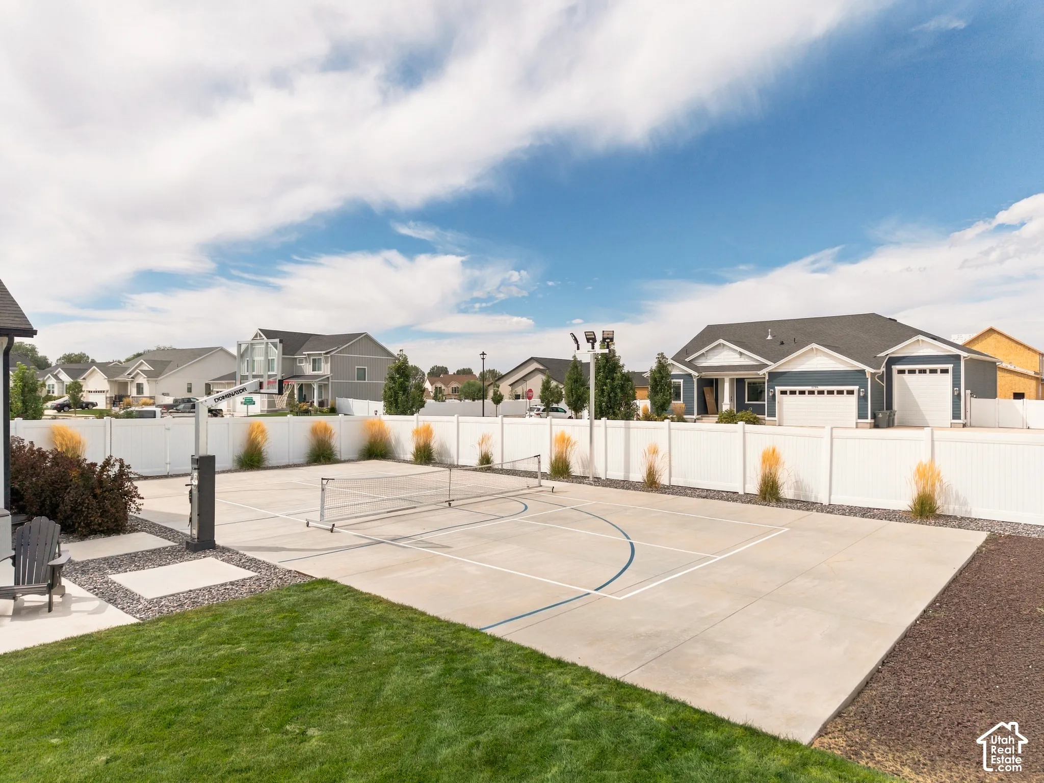 Expansive concrete court with painted lines and a net, surrounded by a white privacy fence