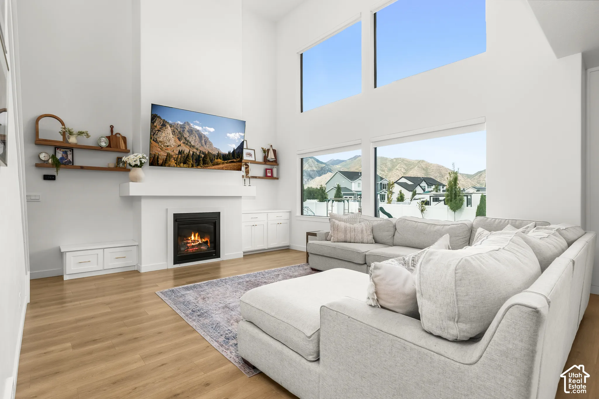 Vaulted ceiling with high windows, gas fireplace, wood-finish flooring, white built-in cabinetry, and large windows showcasing mountain scenery