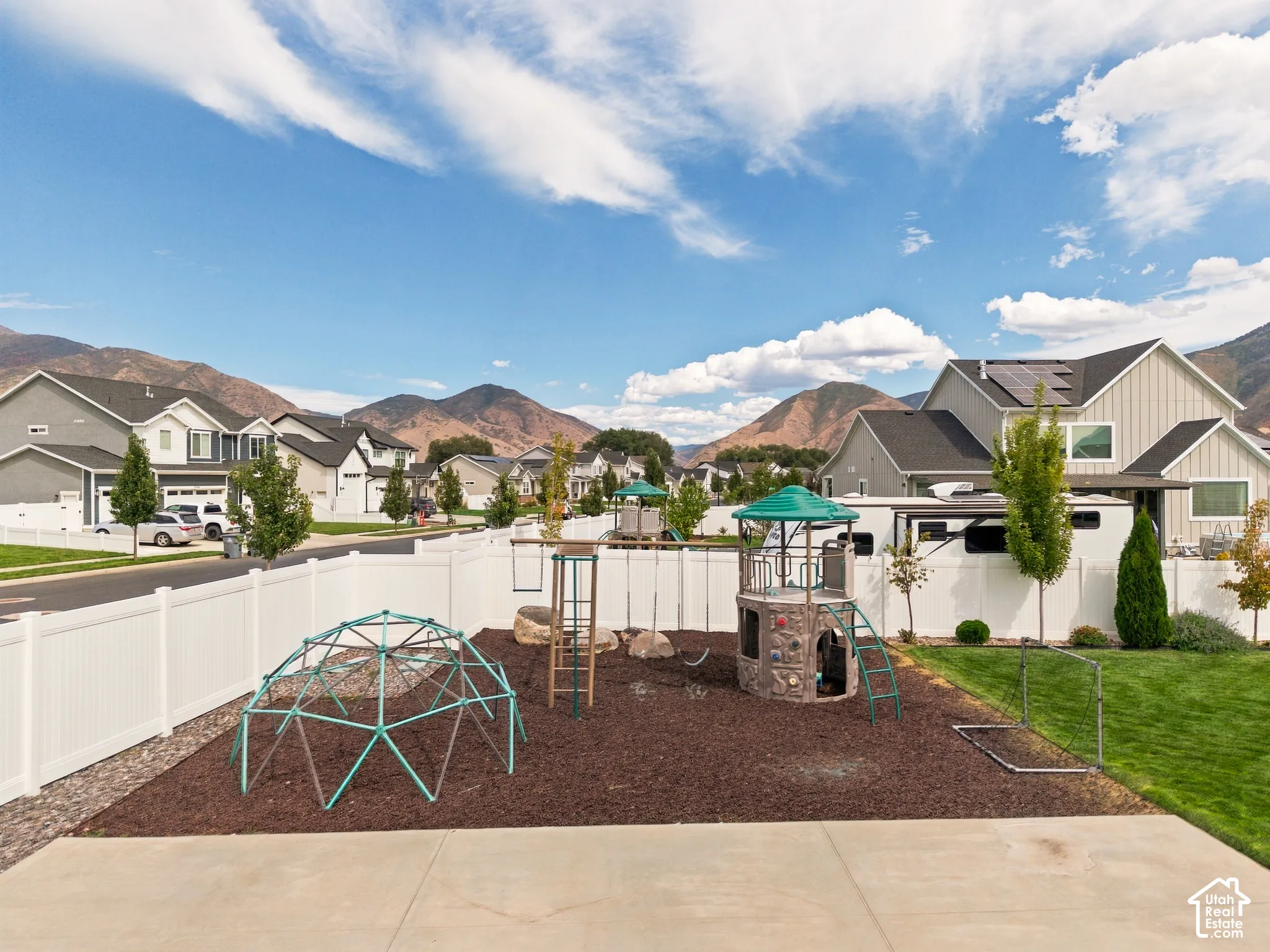Expansive backyard featuring a white vinyl fence, a play structure with a green canopy, and a manicured lawn