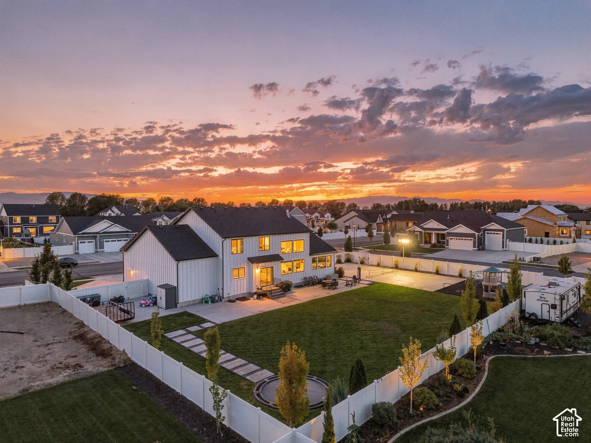 Expansive backyard featuring a large green lawn, concrete patio, and white privacy fencing