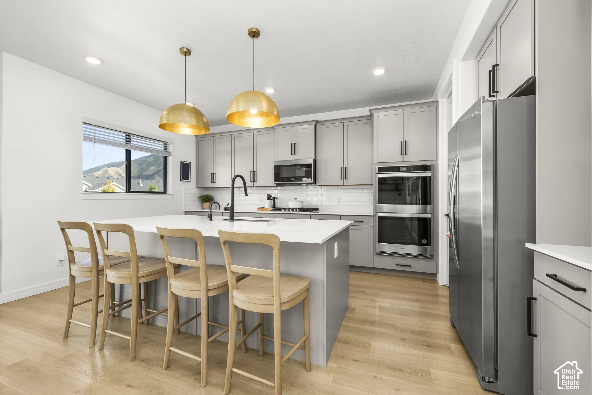 Kitchen featuring a large island with white countertop, gray cabinetry with black hardware, stainless steel appliances, and wood-finish flooring