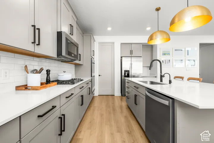 Kitchen featuring a gas range, stainless steel appliances, light wood-finish flooring, and a large island with sink and integrated dishwasher
