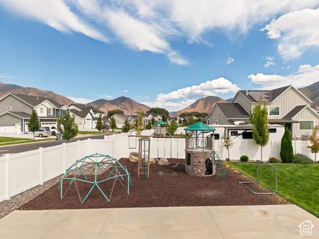 Expansive backyard featuring a white vinyl fence, a play structure with a green canopy, and a manicured lawn