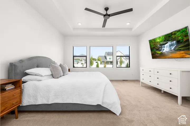 Tray ceiling with recessed lighting, ceiling fan, three windows with dark frames, and carpeted flooring