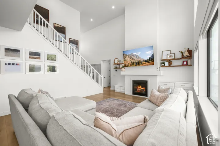 Vaulted ceiling, staircase with white banister, built-in fireplace, wood-finish flooring, and large windows