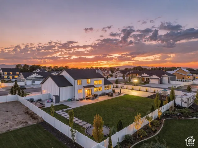 Expansive backyard featuring a large green lawn, concrete patio, and white privacy fencing