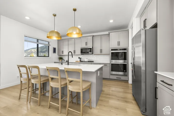Kitchen featuring a large island with white countertop, gray cabinetry with black hardware, stainless steel appliances, and wood-finish flooring