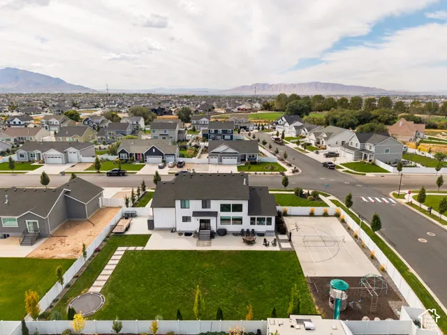 Two-story residence featuring a white vertical siding exterior, an expansive backyard with a manicured lawn, a paved sport court, and a separate play area
