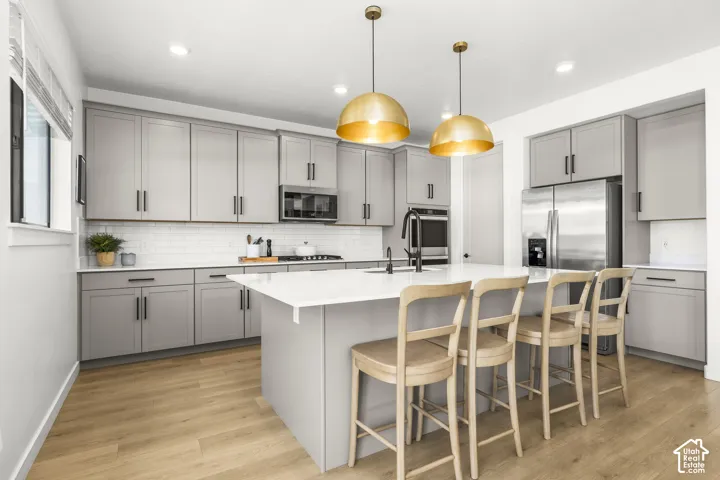 Kitchen featuring light gray cabinetry, stainless steel appliances, a white subway tile backsplash, a large center island with a white countertop, and wood-finish flooring