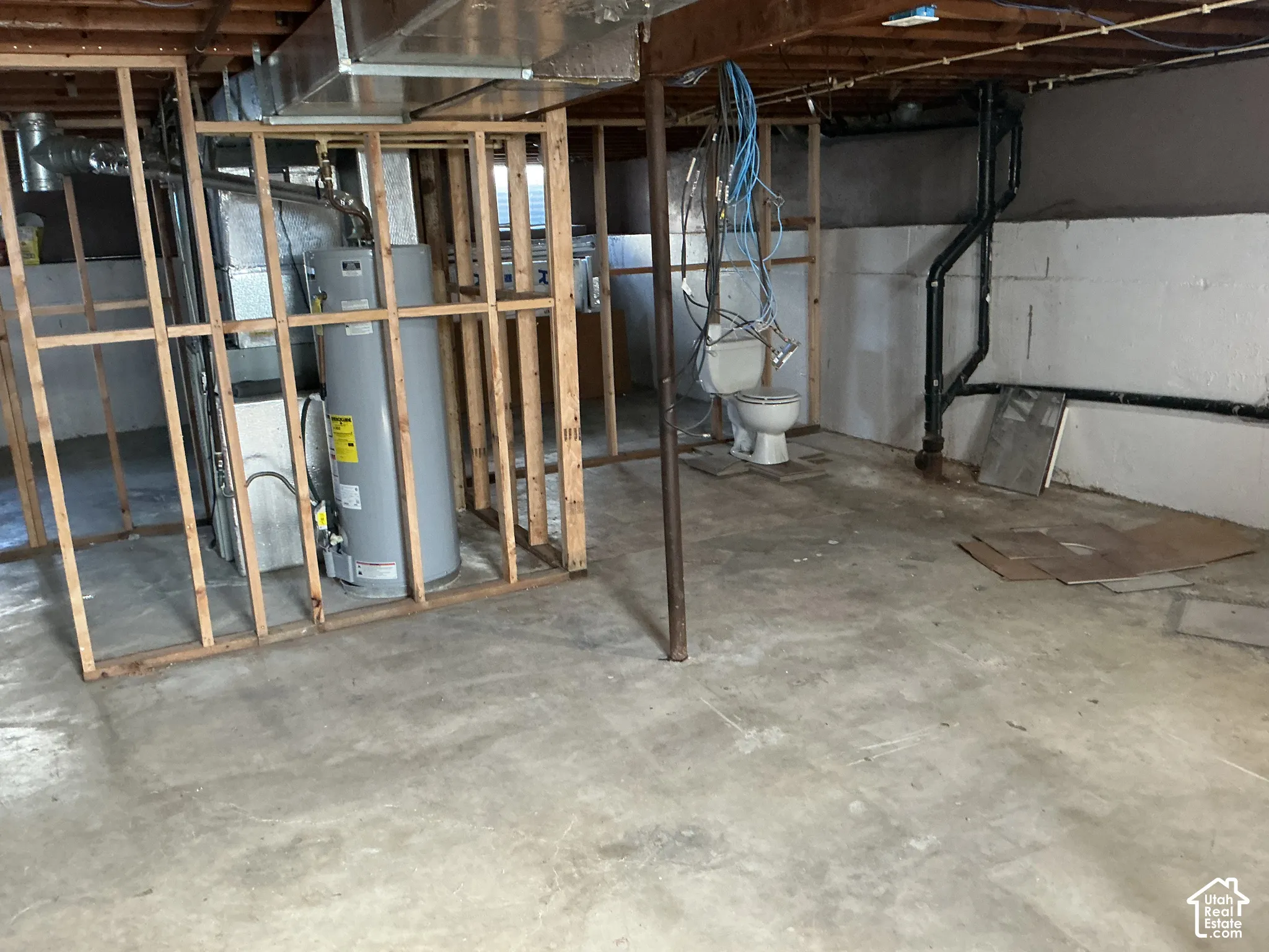 Unfinished basement with concrete flooring, exposed ceiling joists, wood framing, water heater, and an exposed toilet fixture