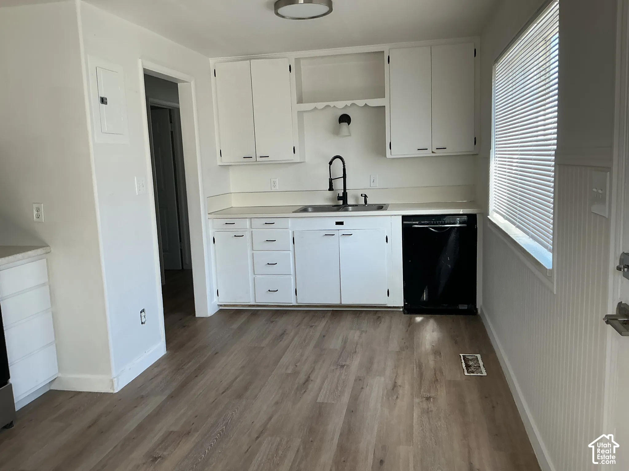 Kitchen featuring wood-finish flooring, white cabinetry, a black dishwasher, and a window with blinds