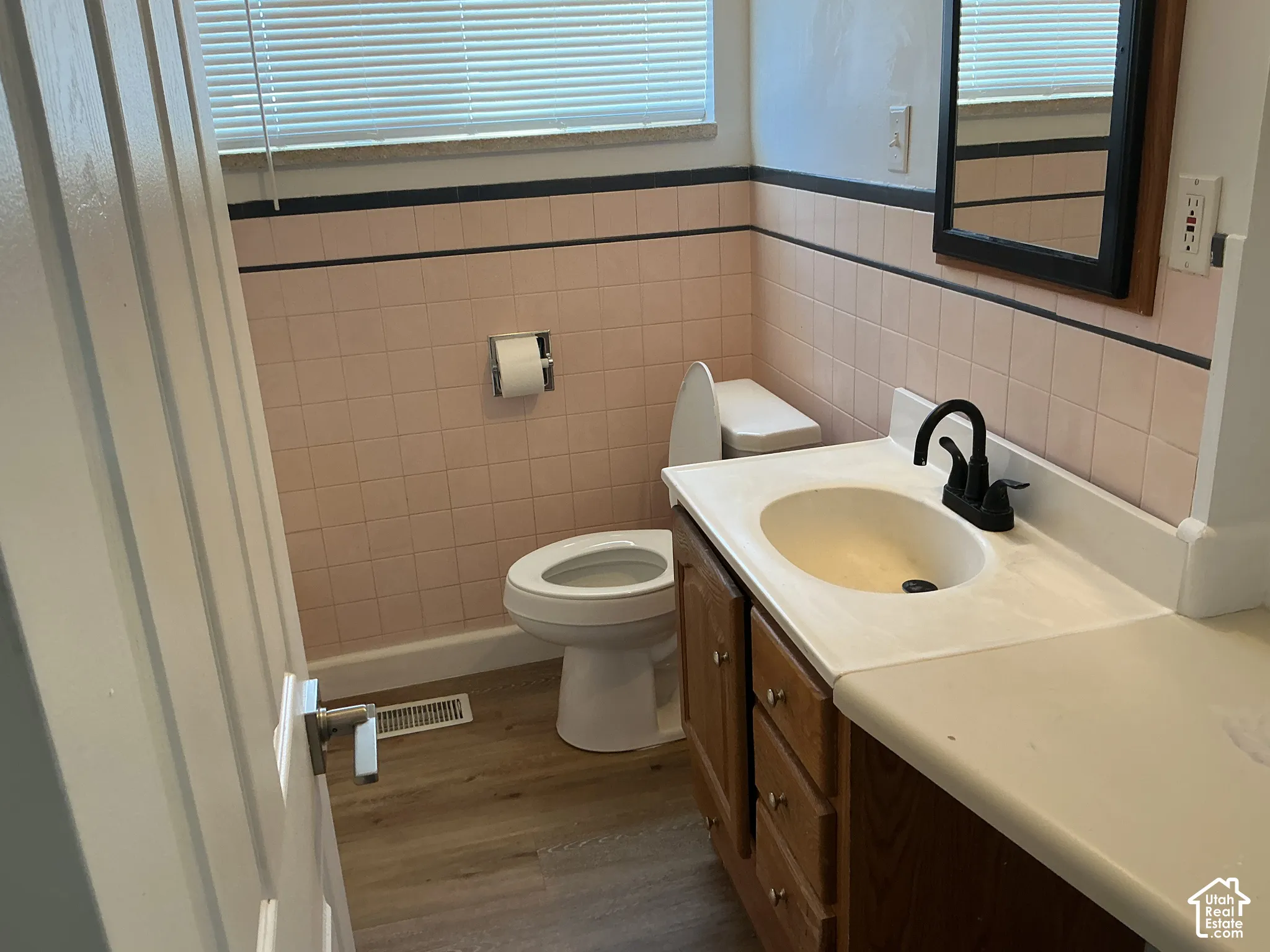 Wood-finish flooring with a white vanity featuring a black faucet and integrated sink