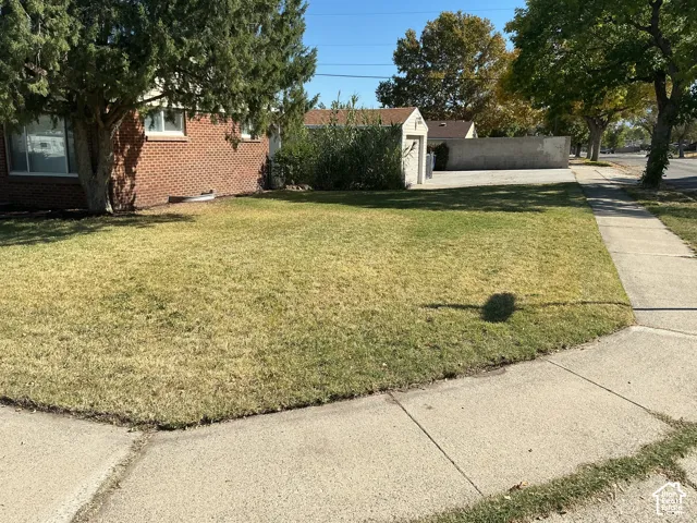 Brick exterior, manicured lawn, established trees, concrete driveway, and concrete sidewalk