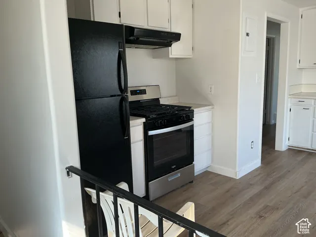 Kitchen featuring white cabinetry, light countertops, black refrigerator, and stainless steel oven with gas range