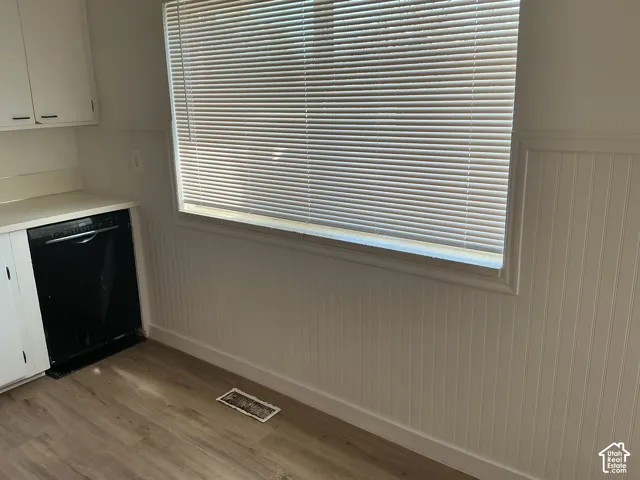 White cabinetry, light wood-finish flooring, a black built-in dishwasher, and a window with horizontal blinds