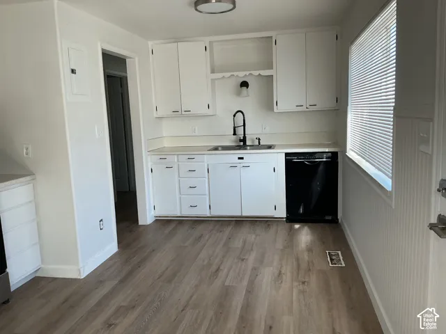 Kitchen featuring wood-finish flooring, white cabinetry, a black dishwasher, and a window with blinds