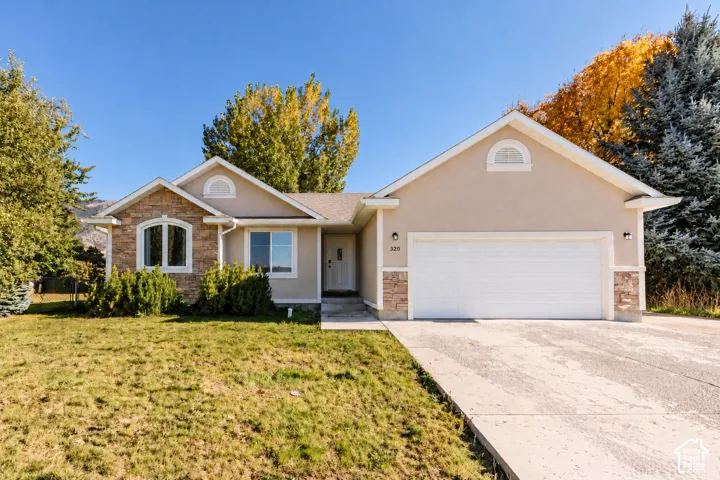 Stucco exterior with stone accents, an arched window, a two-car garage, a concrete driveway, and mature landscaping