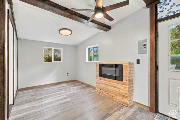 Vaulted ceiling with exposed wood beams, wood-finish flooring, and built-in electric fireplace
