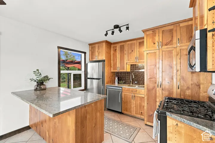 Kitchen featuring wood cabinetry, stainless steel appliances, a center island with a stone countertop, and track lighting