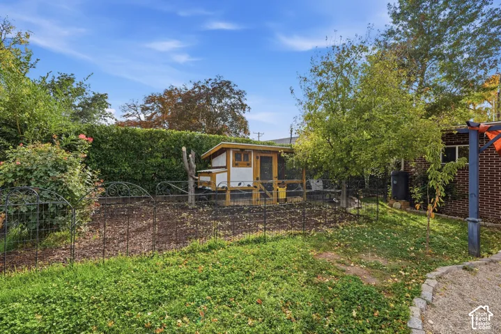 Backyard featuring a chicken coop, cultivated garden area, mature trees, and a brick exterior structure
